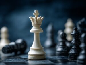 Close-up of a white chess queen surrounded by fallen black chess pieces on a chessboard.