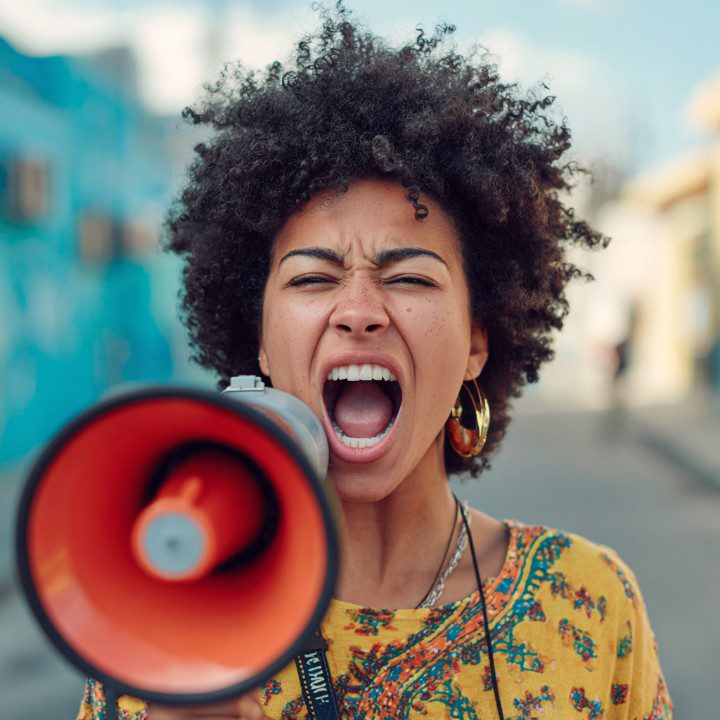 Afro-American woman shouting through a bright orange megaphone in an urban street.