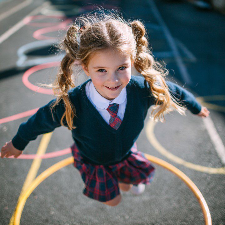 Young schoolgirl in a plaid uniform playing hopscotch outdoors during recess.