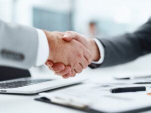 Close-up of two businesspeople shaking hands over a desk with documents and a laptop, symbolizing trust, partnership, and the closing of a business deal.