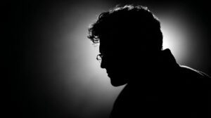 Cinematic silhouette portrait of a man in profile, wearing glasses, captured in black and white with dramatic backlighting.