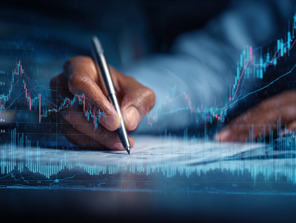 Close-up of businessman writing with financial trading graphs and forex data overlaid, representing investment analysis and economic strategy.