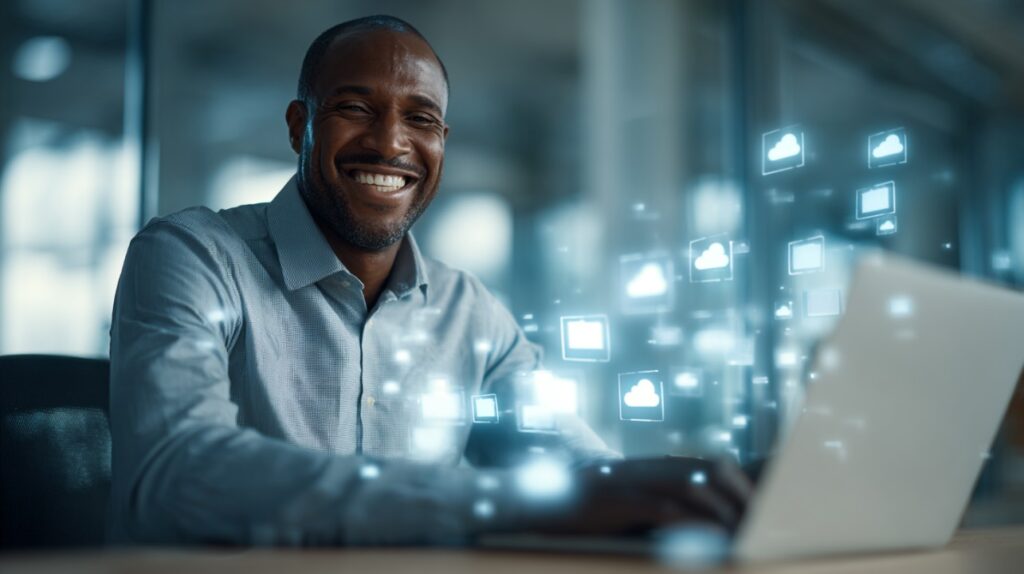 Confident African-American man smiling while working on a laptop with cloud and digital icons floating around, representing modern technology and cloud computing.