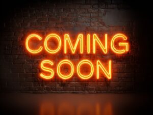 Realistic glowing orange neon sign reading "COMING SOON" on a dark brick wall background.