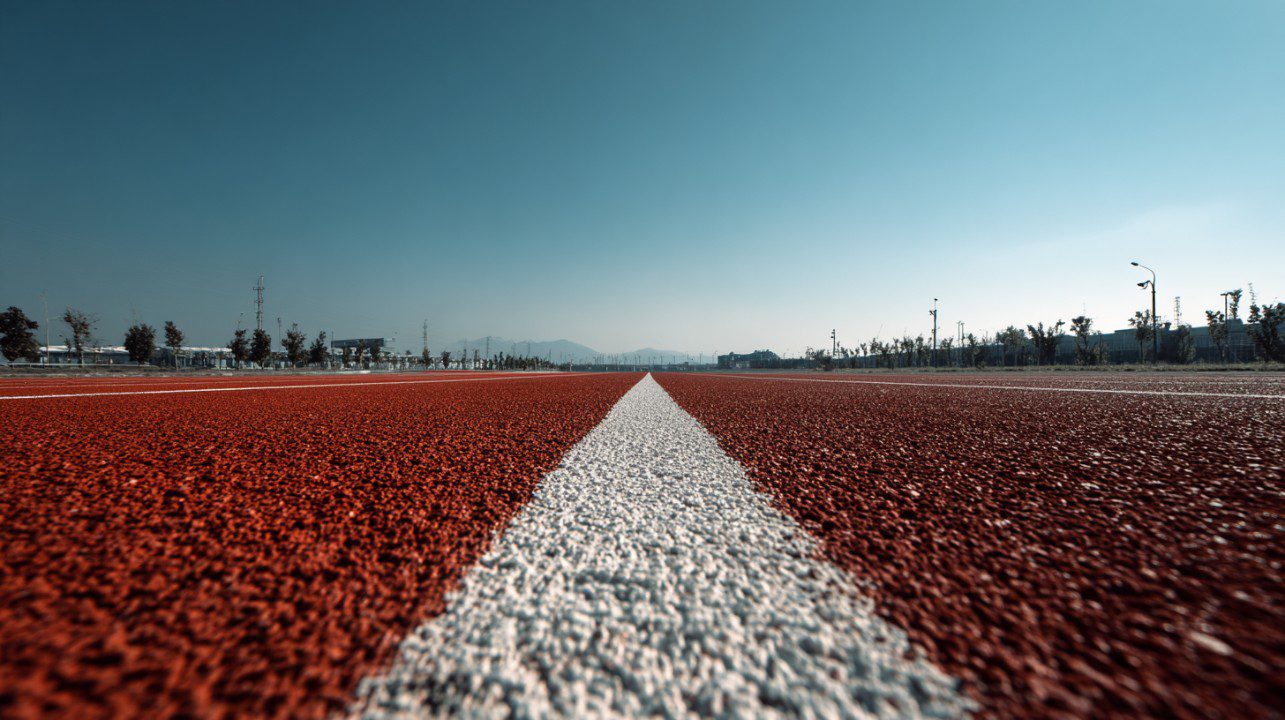 A red running track with a central white line stretching straight into the horizon, symbolizing focus and determination under a clear sky.
