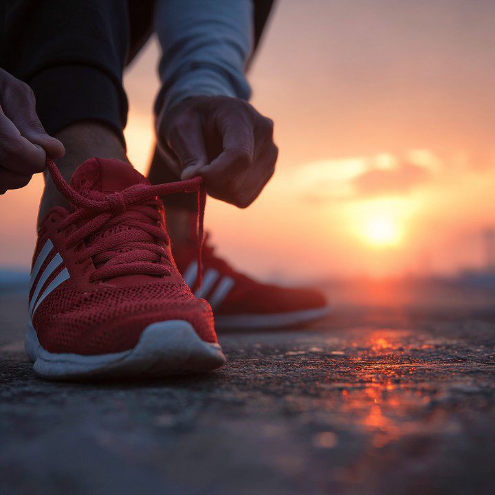 Close-up of a person tying red sneakers on a pavement at sunrise, symbolizing motivation and a healthy start to the day.
