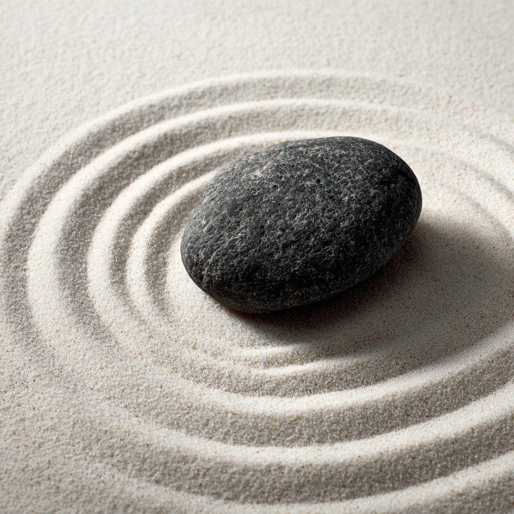 Smooth dark stone resting in raked white sand with concentric circles, evoking a sense of calm, balance, and mindfulness.