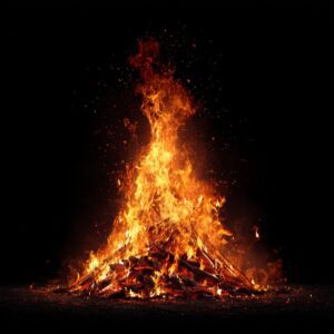 Tall bonfire with vivid orange flames and sparks rising against a solid black background, creating a dramatic and energetic scene.