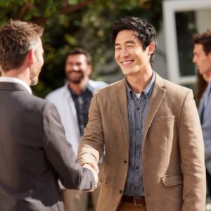 Two business professionals shaking hands outdoors during a networking event, representing collaboration, trust, and partnership.