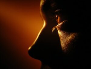 Extreme close-up of a human face in silhouette illuminated by a warm orange light, emphasizing emotion, texture, and atmosphere.