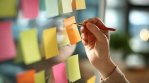 Person writing on colorful sticky notes during a brainstorming session, representing creativity, planning, and team collaboration.