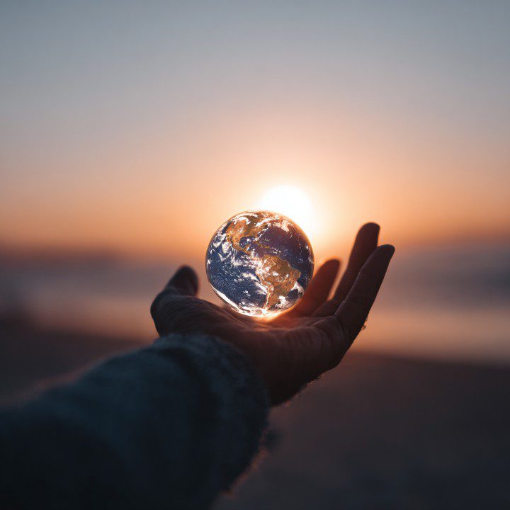 A hand holding a glowing Earth with a sunset in the background, symbolizing global unity, environmental care, and human responsibility.