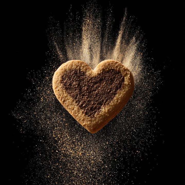 Heart-shaped cookie with chocolate center and golden baking dust against black background.