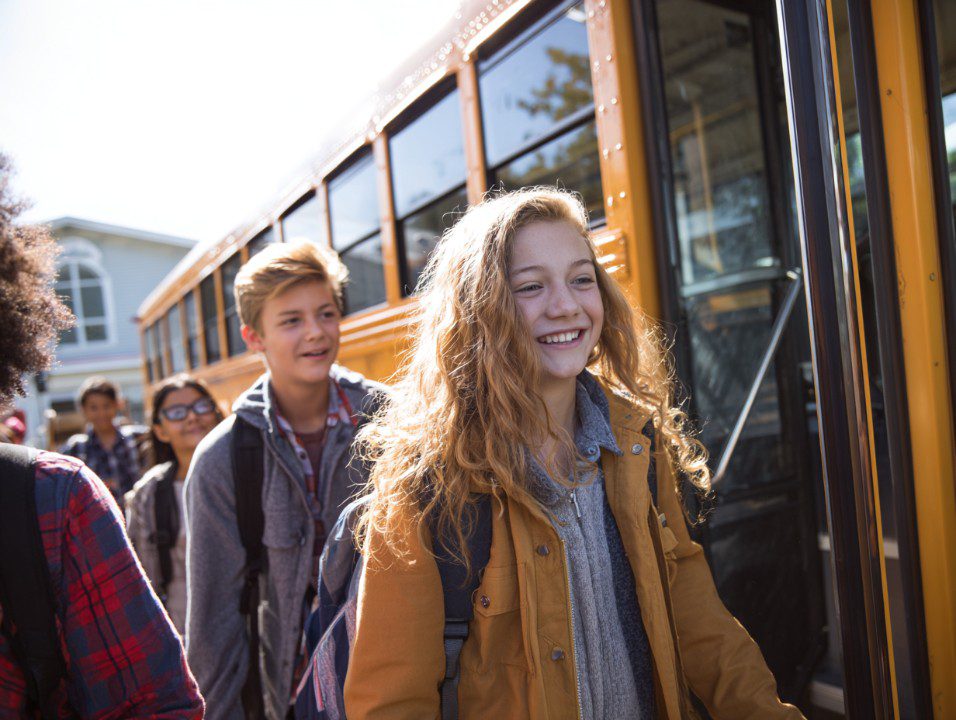 Group of smiling middle school students stepping off a yellow school bus in the morning.