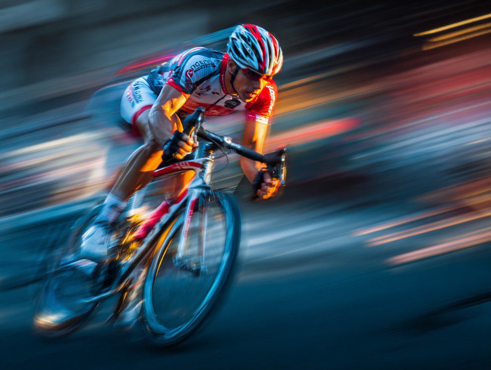 A professional cyclist in a red and white racing outfit speeds through a competition with motion blur highlighting the intensity and velocity.