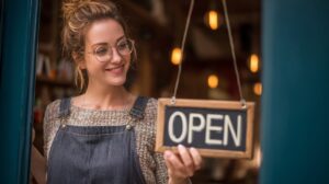 Smiling woman holding an open sign at her shop entrance, representing entrepreneurship, customer service, and the joy of running a small business.