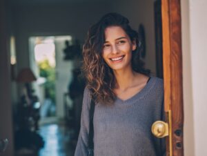 Young woman smiling warmly as she enters her cozy home, radiating happiness and comfort in a relaxed lifestyle setting.