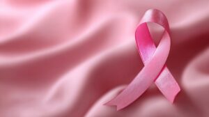 A 3D pink breast cancer awareness ribbon placed on soft pink fabric, symbolizing support, hope, and health awareness.
