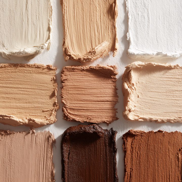 Overhead macro shot of creamy foundation swatches in various natural skin tones, arranged in a flatlay for inclusive beauty representation.