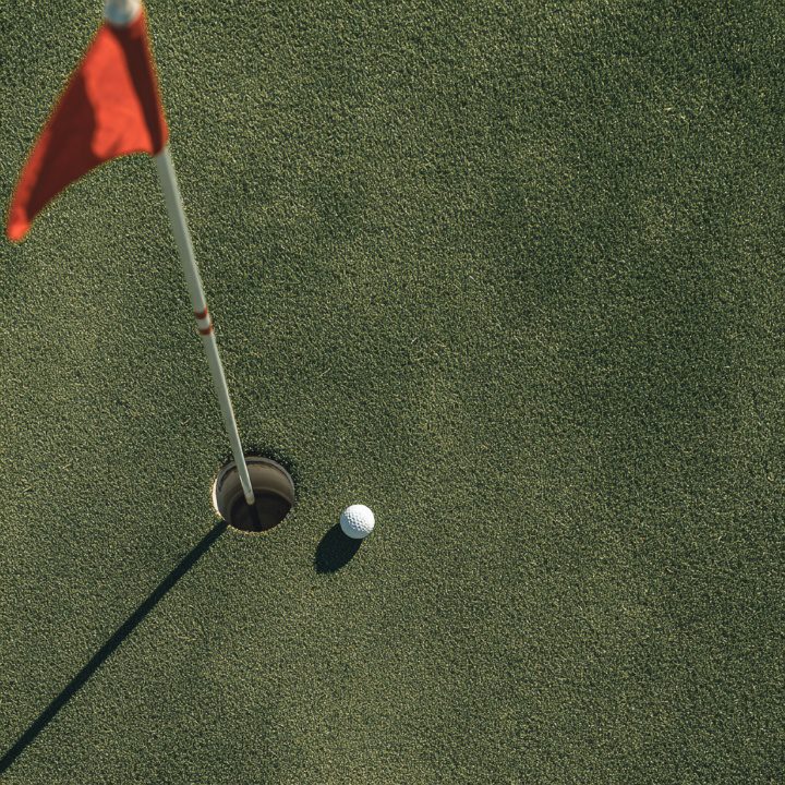 High-angle view of a golf ball near the hole with a red flag on a manicured green.