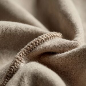 Close-up of soft beige fabric folds with visible stitching, showing a warm textile texture and clean neutral tones.