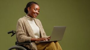 Smiling woman in a wheelchair using a laptop, representing accessibility, inclusion, and modern digital independence.